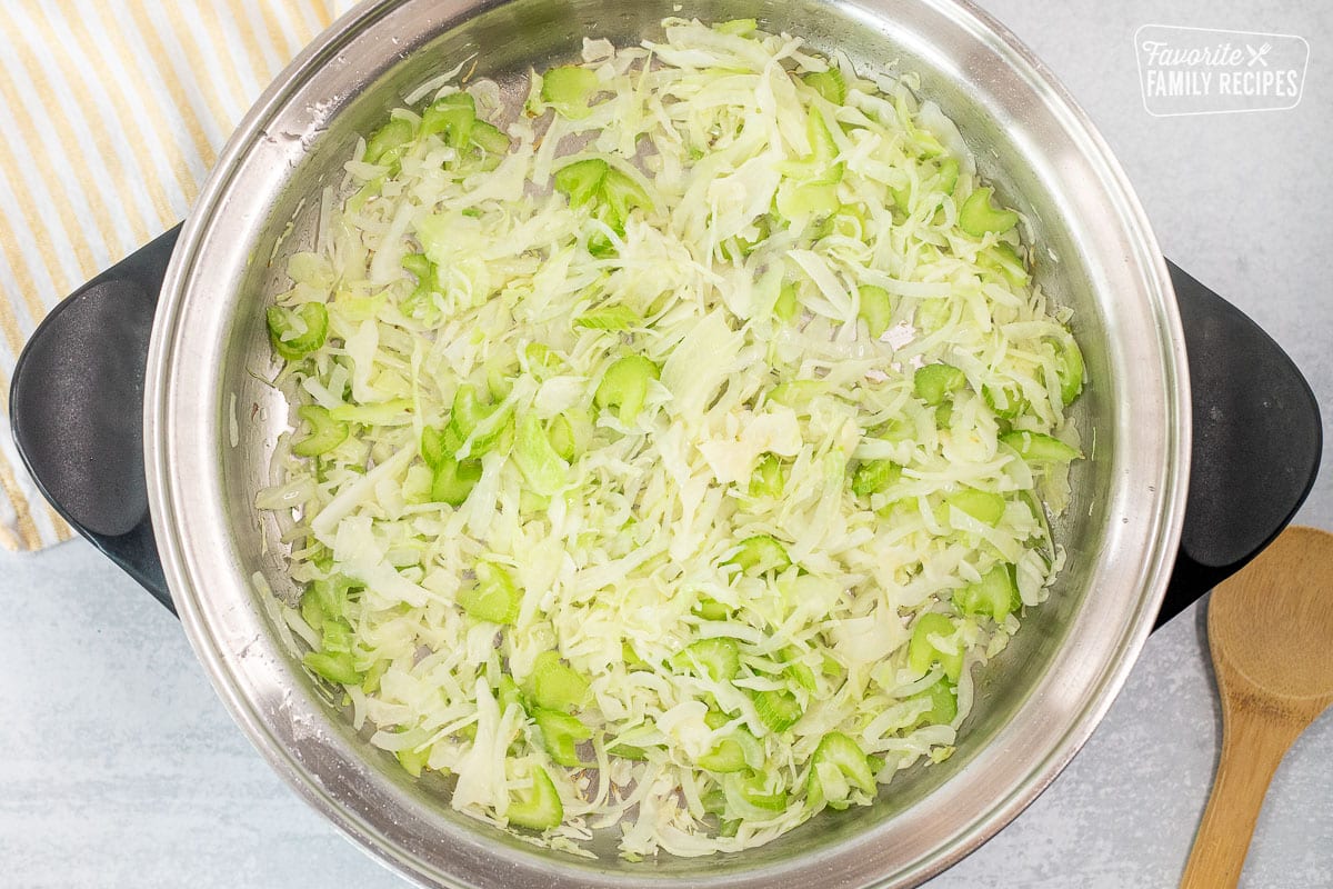 Large skillet with cooked onion, cabbage and celery. Wooden spoon on the side.