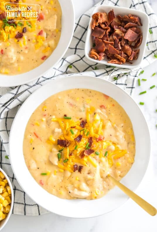 a bowl of chicken corn chowder topped with cheese, bacon, and chives