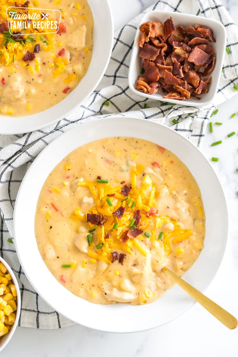 a bowl of chicken corn chowder topped with cheese, bacon, and chives