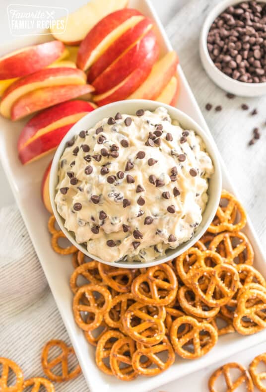 a bowl of chocolate chip cookie dough dip on a platter with pretzel twists and apple slices