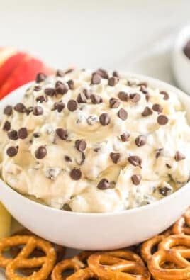 a bowl of chocolate chip cookie dough dip on a platter with pretzel twists and apple slices