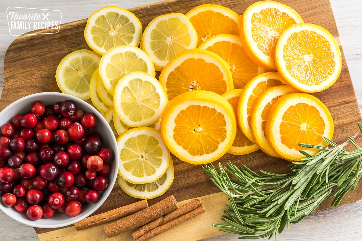 lemon slices, orange slices, cinnamon sticks, rosemary sprigs, and cranberries on a cutting board