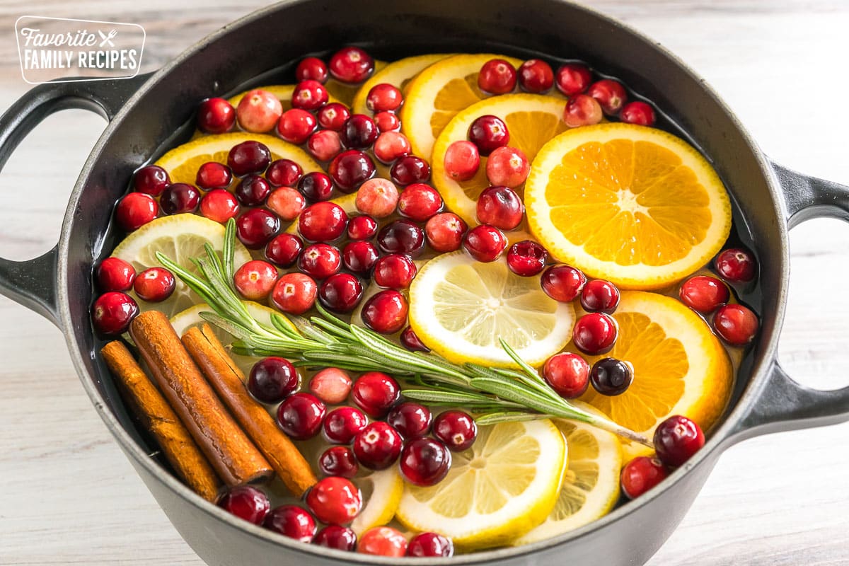 a pot filled with lemon slices, orange slices, cinnamon sticks, rosemary sprigs, cranberries, and water