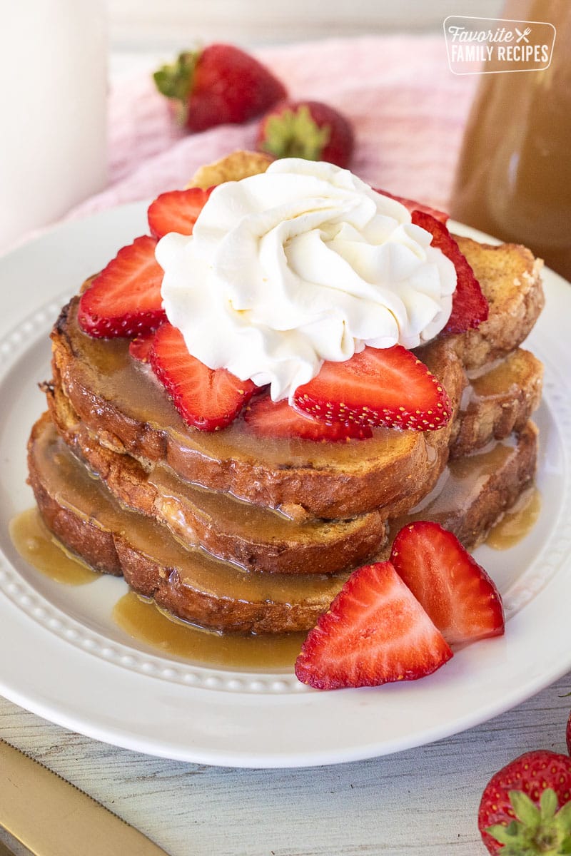 Plate with three slices of Cinnamon French Toast topped with syrup, strawberries and cool whip.