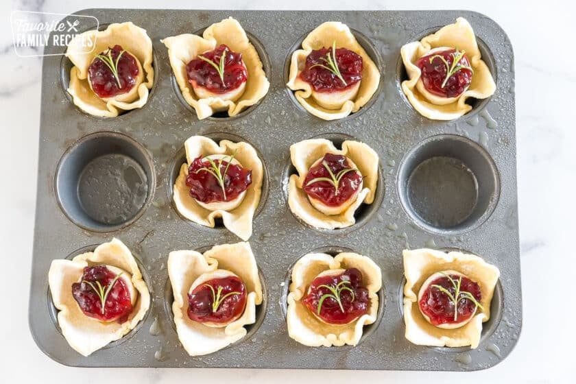 squares of puff pastry with mini brie, cranberry sauce, and rosemary sprigs in a muffin tin before being baked