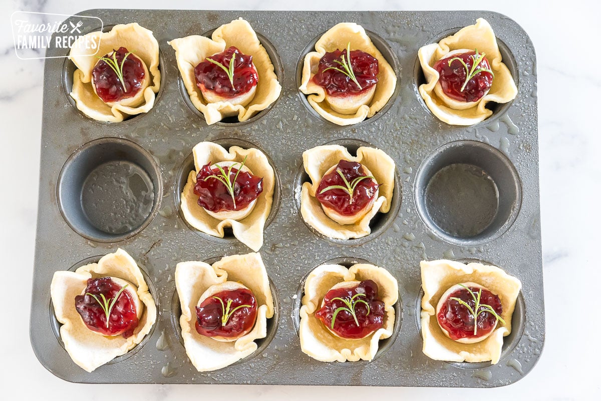 squares of puff pastry with cheese, fruit spread, and rosemary sprigs in a muffin tin before being baked