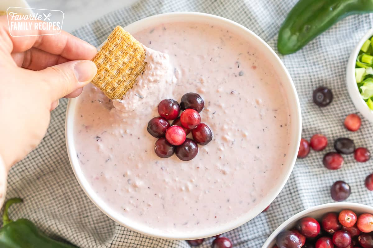 a bowl of cranberry jalapeno dip topped with cranberries with a cracker dipping into it