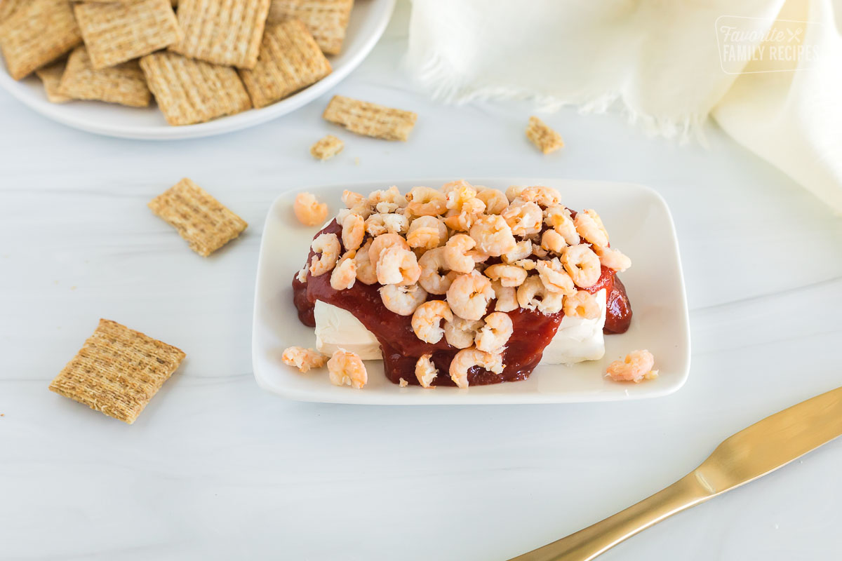 Cream cheese shrimp dip, a plate of crackers and a knife all laid out on the table.