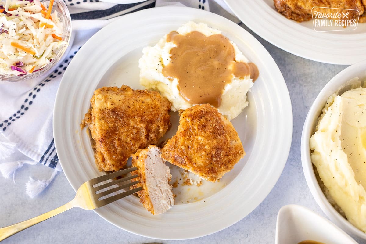 Plate with cut piece of Oven Fried Chicken next to mashed potatoes with gravy.