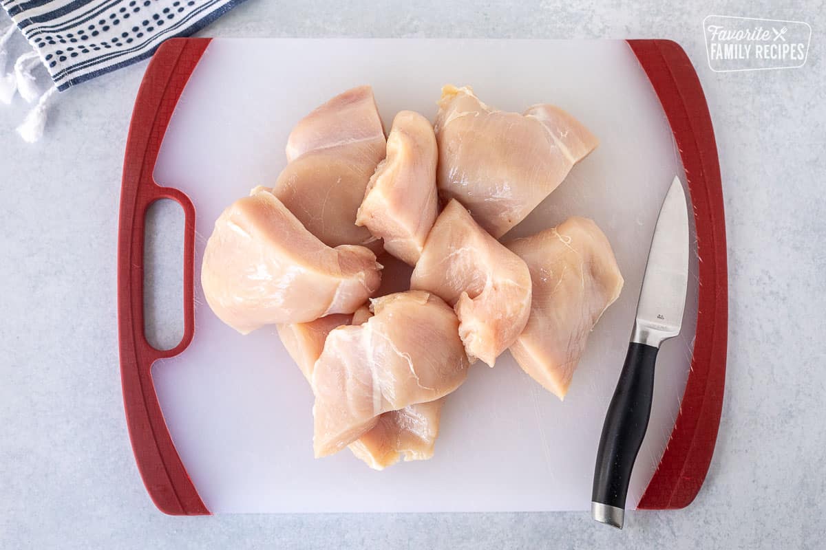 Cutting board with chicken breasts cut in half with knife on the side.