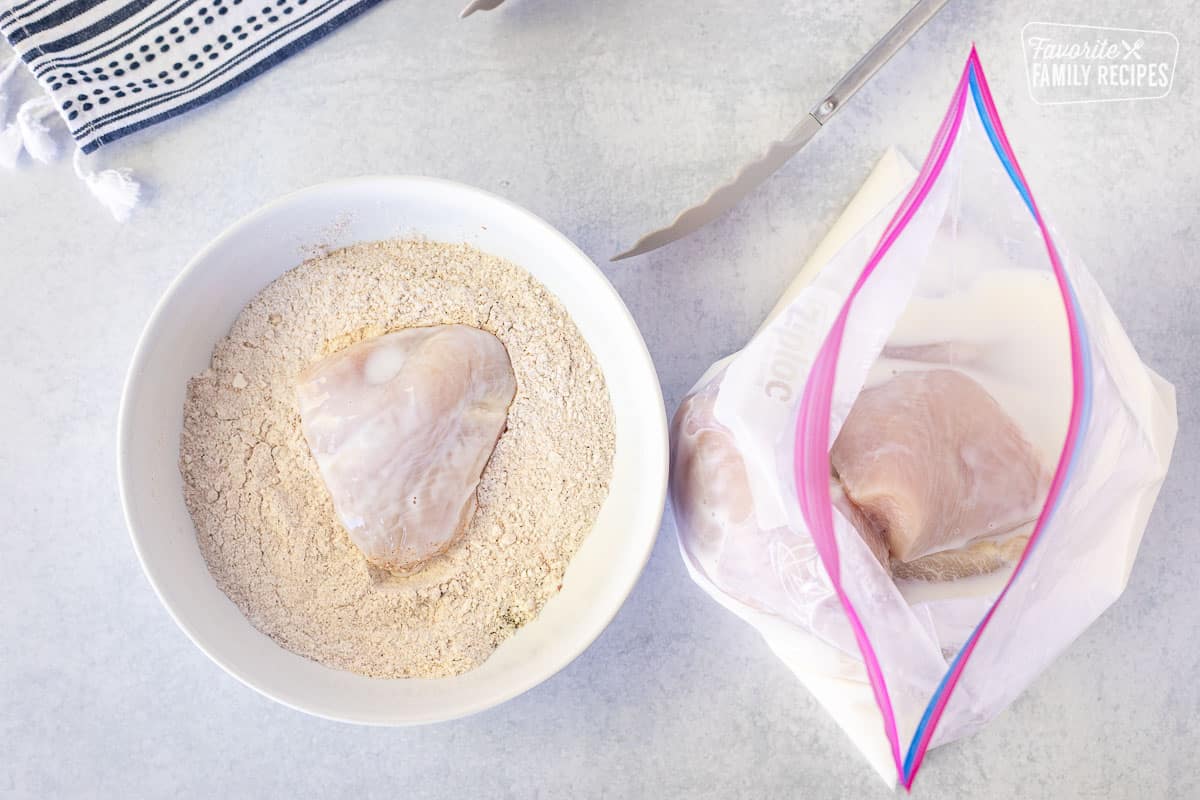 Piece of chicken breast in a bowl of flour mixture next to bag of chicken breast in buttermilk.