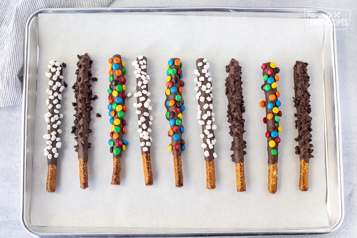 Baking sheet with drying Dipped Pretzel Rods topped with mini mnm's, marshmallow bits and mini chocolate chips.