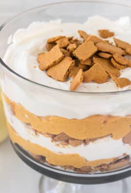 An angled view of easy pumpkin trifle with layers of whipped cream, pumpkin cheesecake, and gingersnap cookies.