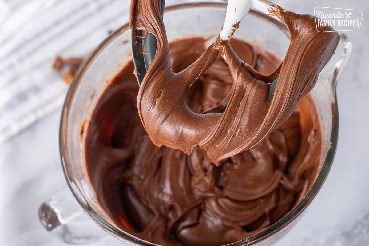 Paddle with smooth chocolate fudge held above mixing bowl.