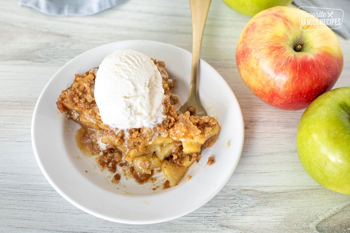 Gluten Free Apple Pie on a plate with a fork cutting into it. Vanilla ice cream on top and melted a little into the pie.