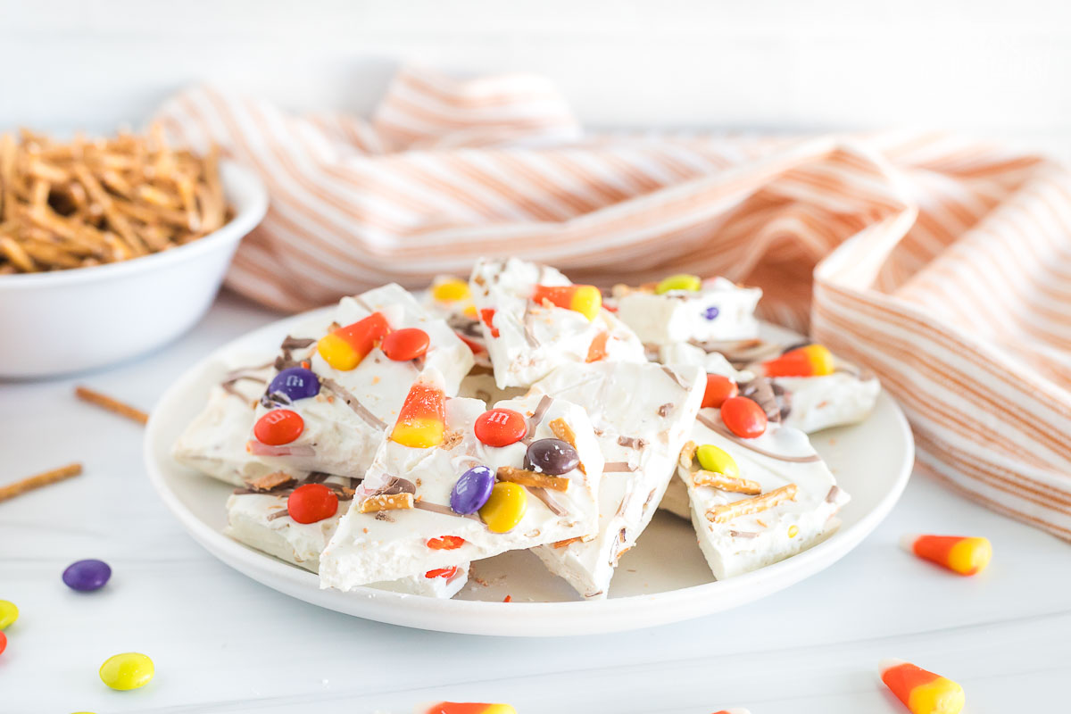 A plate filled with pieces of halloween candy bark, containing candy corn, pretzels, m&m's, reese's pieces, and butterfingers.