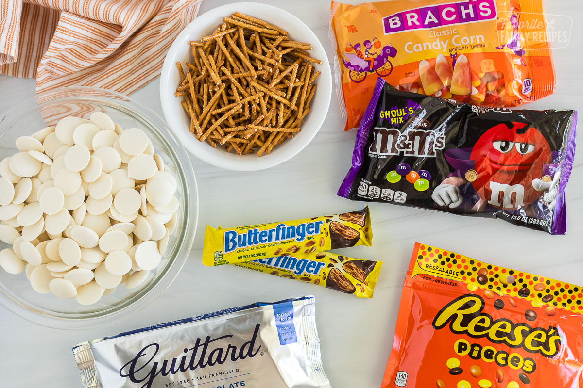 Ingredients for Halloween Candy Bark, including white chocolate melts, pretzels, candy corn, m&m's butterfingers, reese's pieces, and chocolate chips.