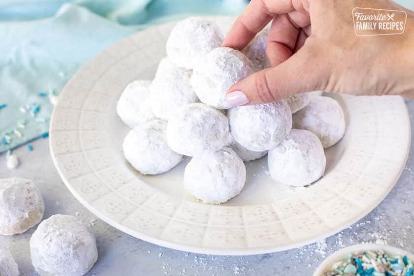 Hand grabbing a Snowball cookie from a plate.
