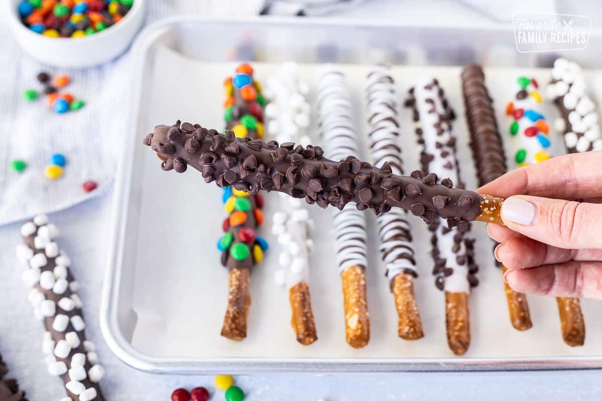 Hand holding a pretzel rod dipped with chocolate and decorated with mini chocolate chips.