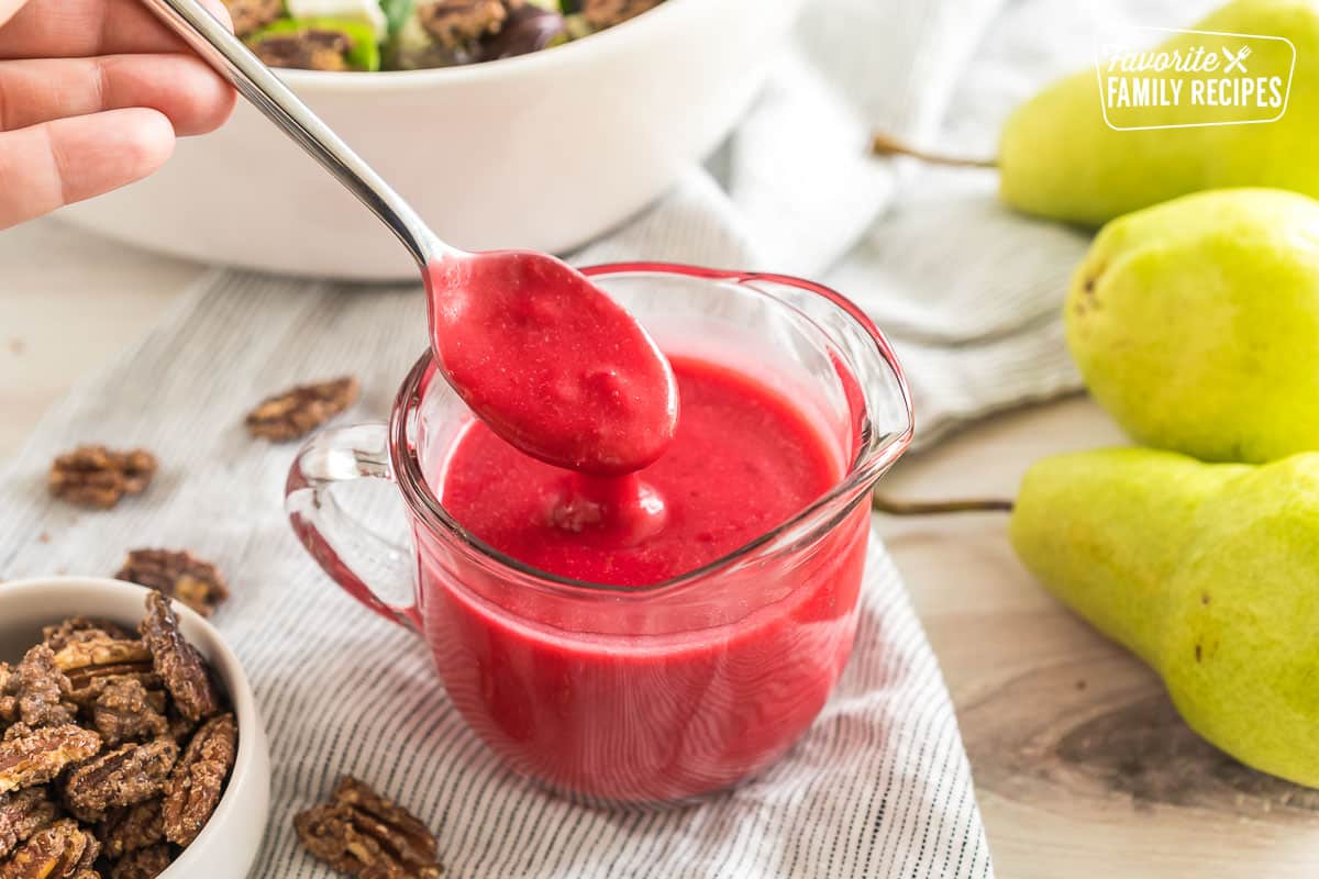 Cranberry Vinaigrette Dressing in a small glass pitcher with a spoon taking a spoonful