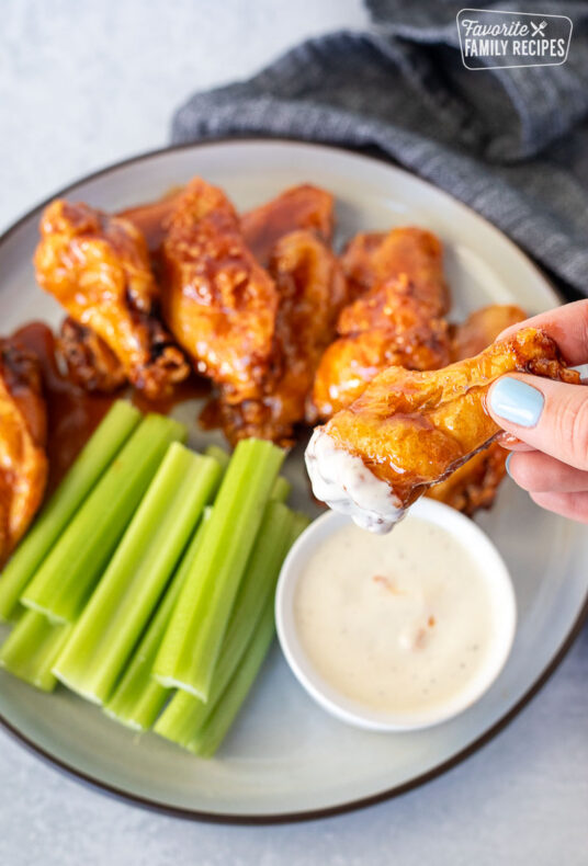 Hand holding a Winger's Wing with Freakin Amazing Sauce dipped in ranch.