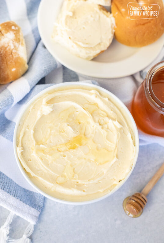 Bowl of Homemade Honey Butter next to honey and rolls.