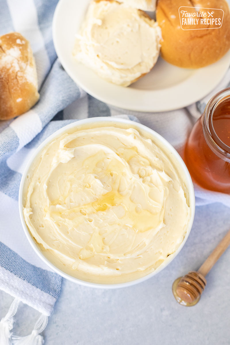 Bowl of Homemade Honey Butter next to honey and rolls.