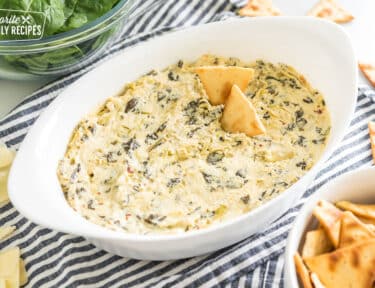 spinach artichoke dip in an oval baking dish with pita chips