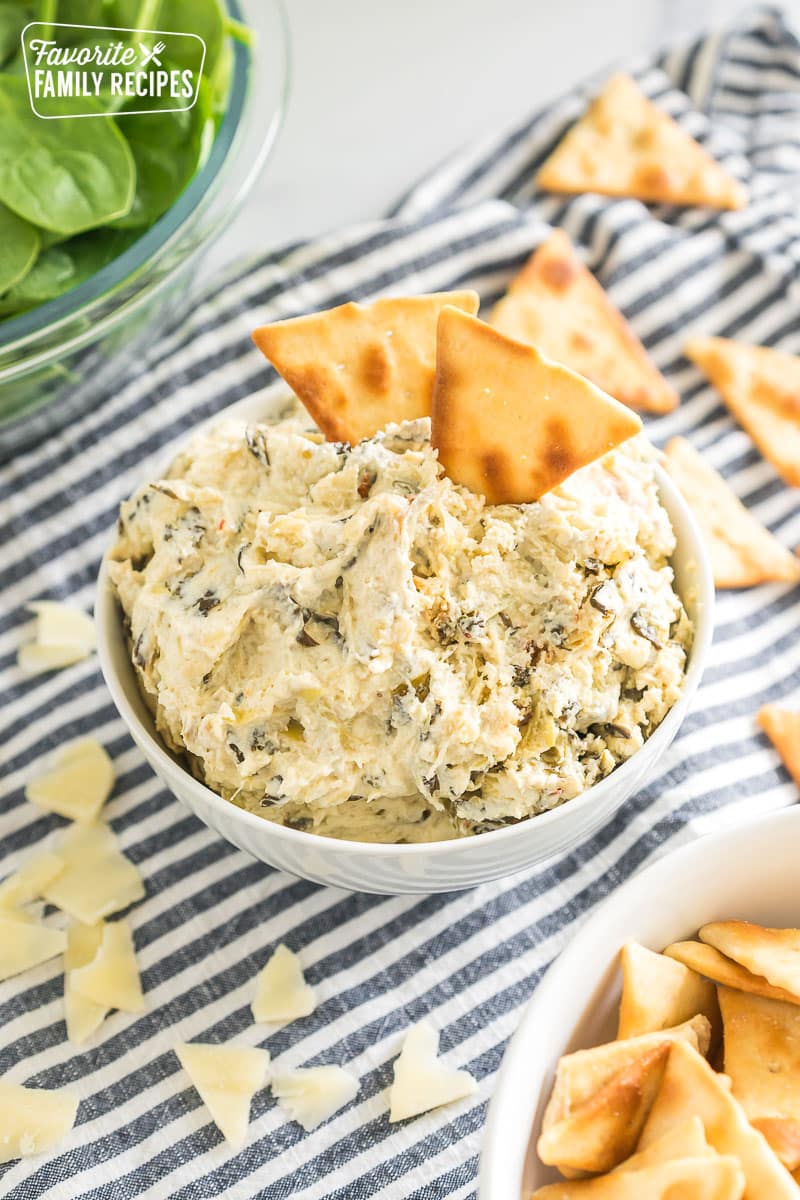 two pita chips in a small bowl of spinach artichoke dip