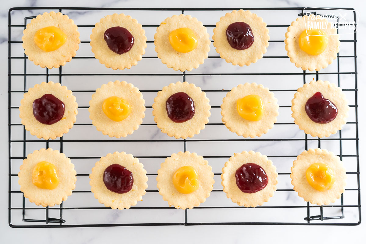shortbread circles topped with jam and lemon curd on a wire rack