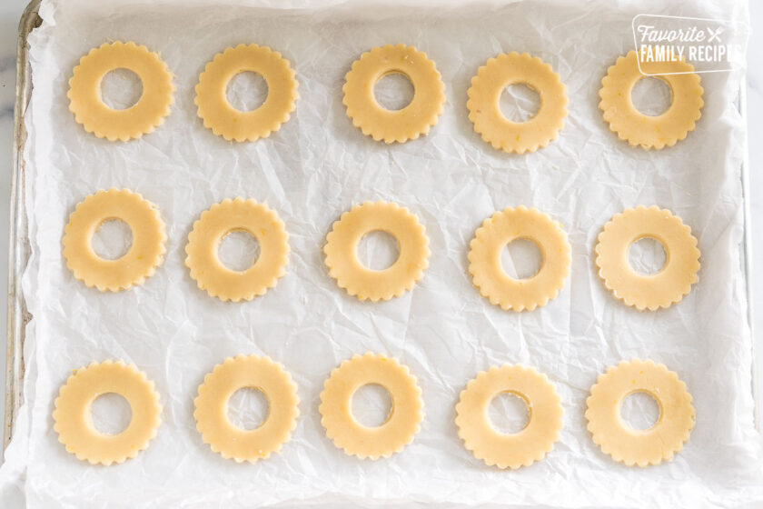 shortbread dough cut into circles with scalloped edges with holes in the middle on a baking sheet