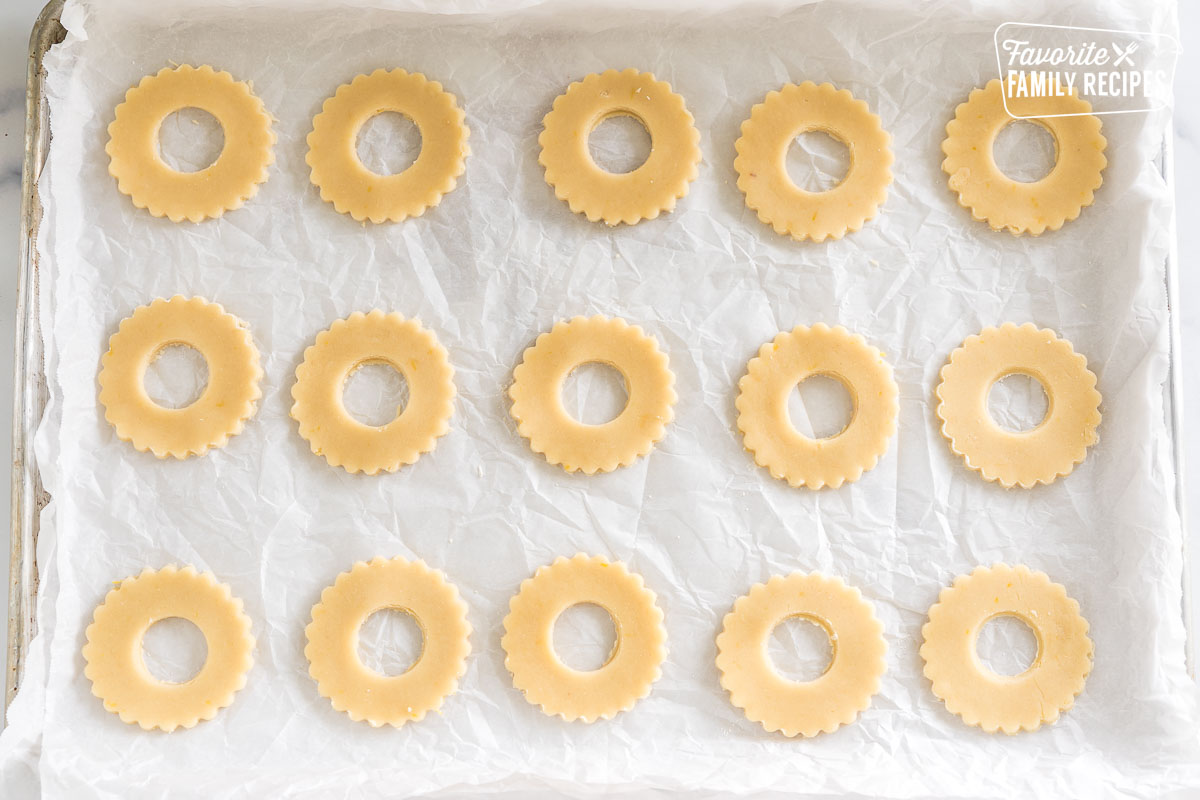 shortbread dough cut into circles with scalloped edges with holes in the middle on a baking sheet