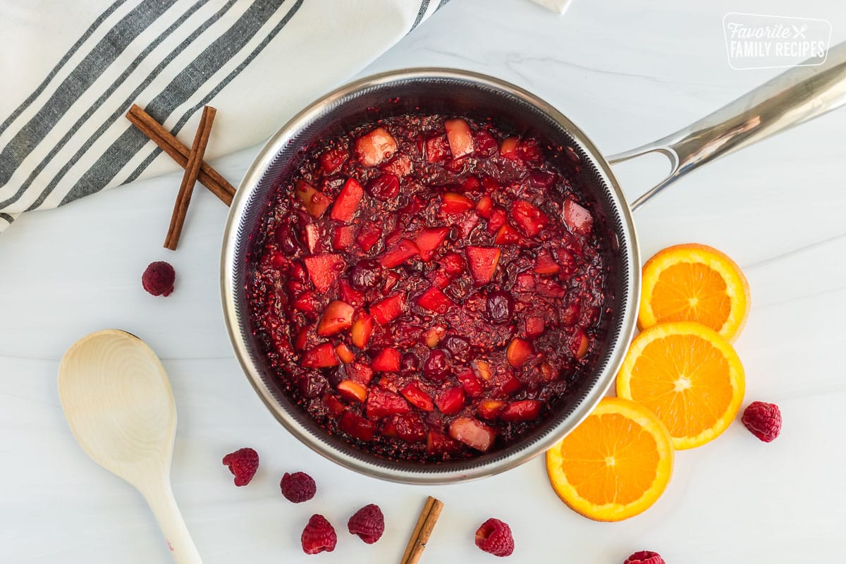 Low Sugar Cranberry Sauce in a saucepan that has been thickened and cooked on the stove. Pieces of oranges, apples, cranberries and raspberries can be seen within the sauce.