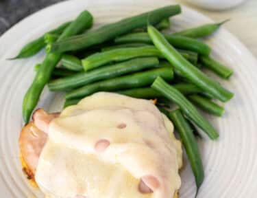 Slice of Malibu Chicken on a plate with green beans and dish of sauce on the side.