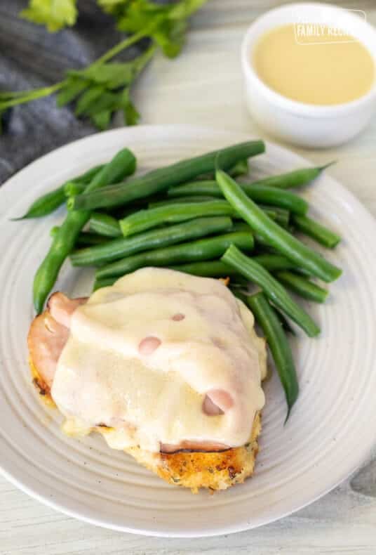 Slice of Malibu Chicken on a plate with green beans and dish of sauce on the side.