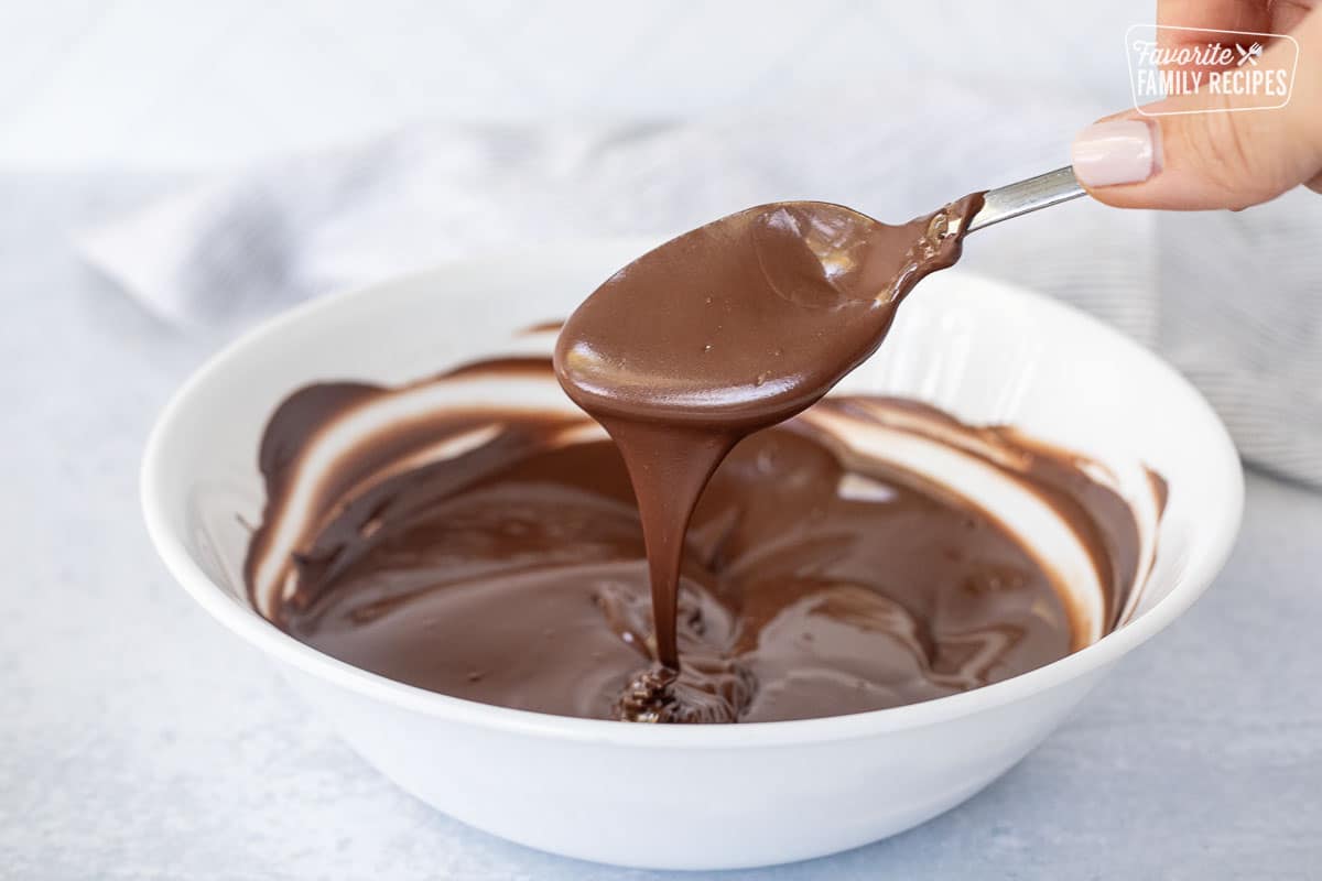Spoon dripping melted milk chocolate into a bowl.