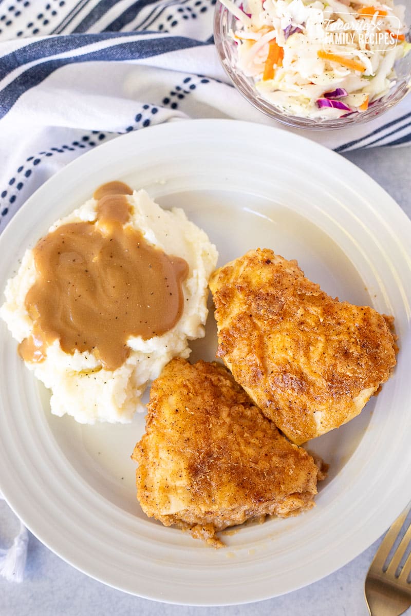Plate with two pieces of Oven Fried Chicken and mashed potatoes with gravy.