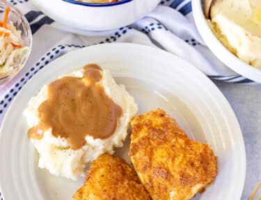 Plate with two pieces of Oven Fried Chicken, Mashed potatoes and gravy.