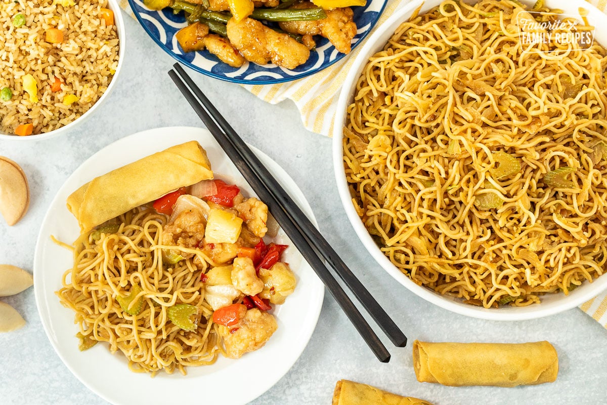 Plate of Panda Express Chow Mein Noodles with chicken pineapple next to a bowl of chow mein noodles, rice and rolls.