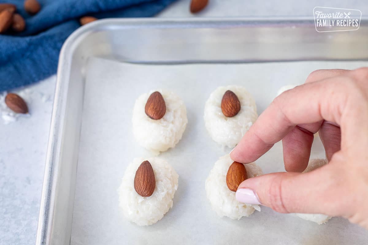 Hand placing almonds on top of oval-shaped coconut mixtures.