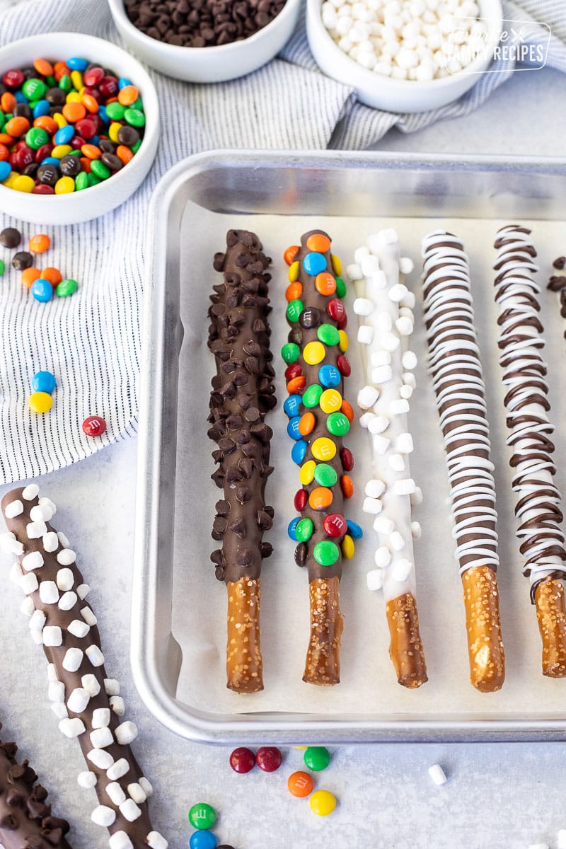 Baking sheet with chocolate dipped pretzel Rods decorated with mini chocolate chips, mini mnm's, chocolate swirls and marshmallow bits.