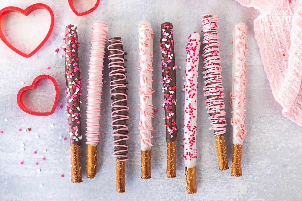 Lined up Valentine's Day Dipped Pretzel Rods decorated with chocolate swirls and sprinkles.