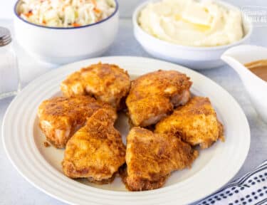 Plate of Oven Fried Chicken next to sides of Cole slaw, mashed potatoes and gravy.