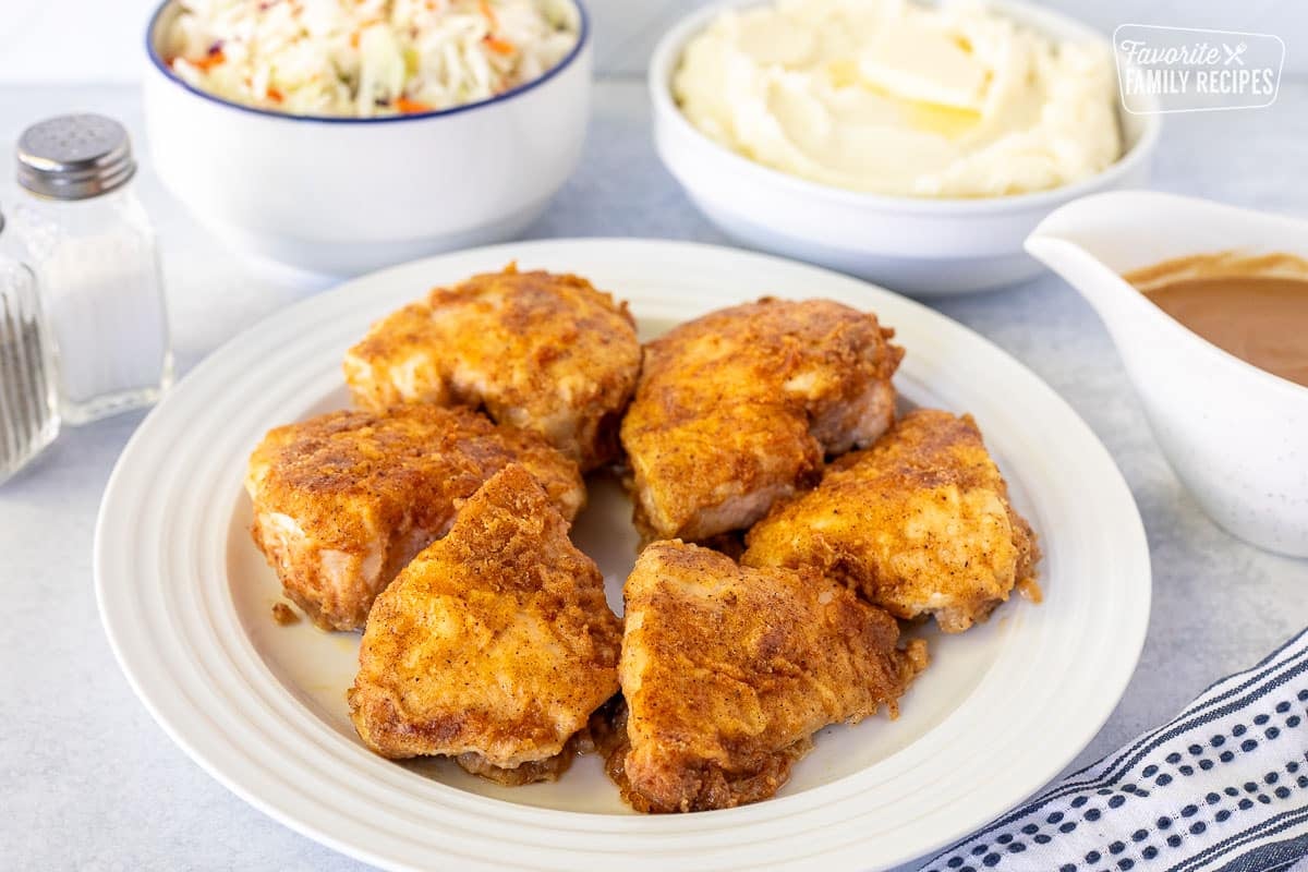 Plate of Oven Fried Chicken next to sides of Cole slaw, mashed potatoes and gravy.