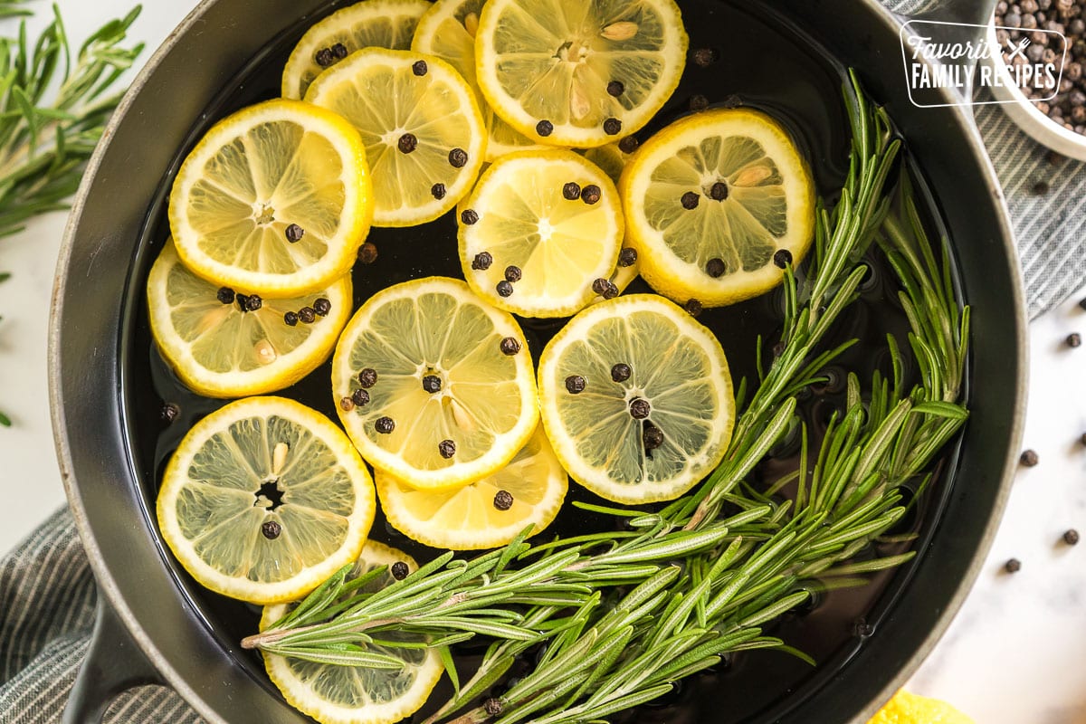 A pot filled with water, lemon slices, peppercorns, rosemary sprigs, and vanilla extract