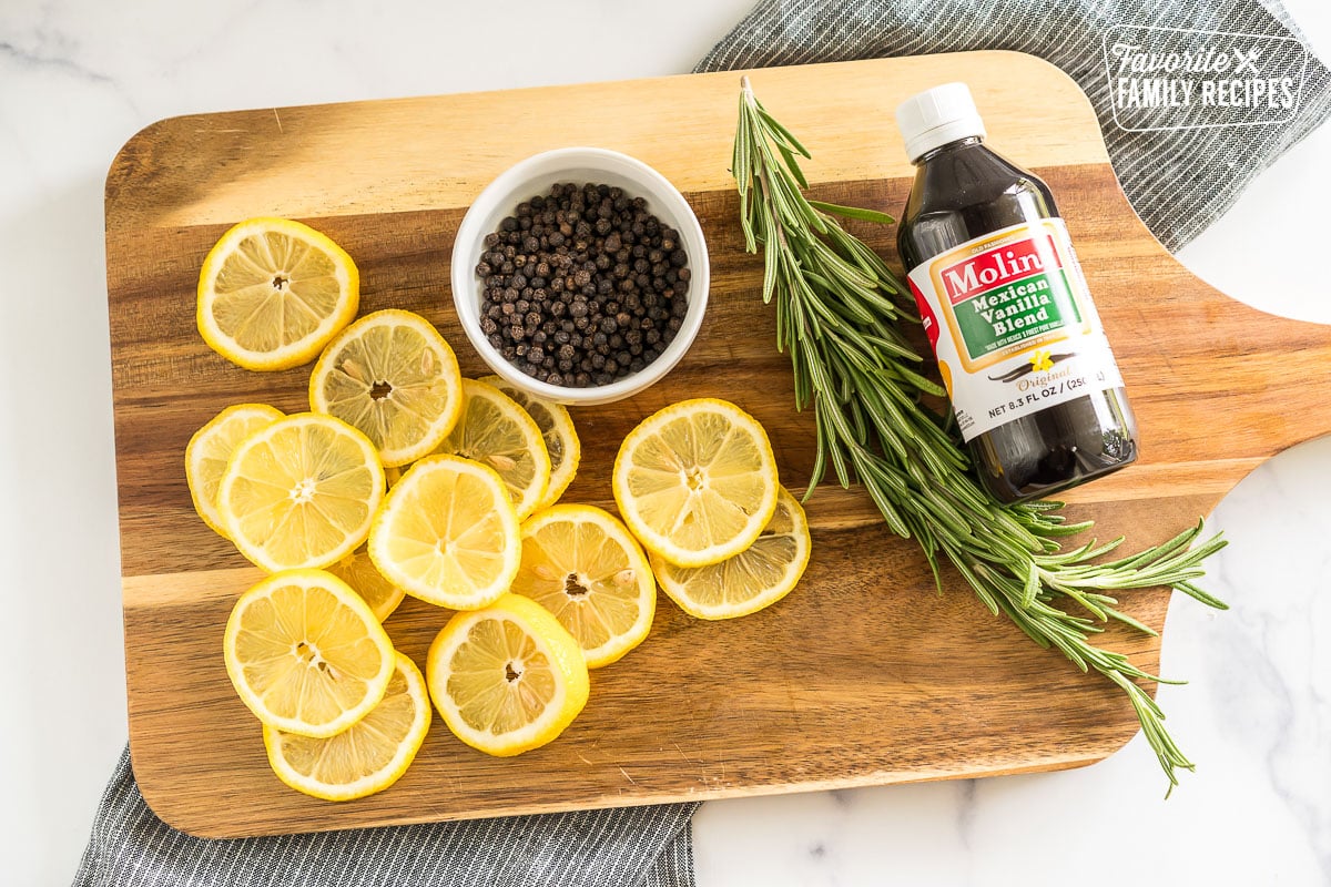 lemon slices, peppercorns, rosemary sprigs, and vanilla extract on a cutting board
