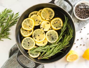 A pot filled with water, lemon slices, peppercorns, rosemary sprigs, and vanilla extract
