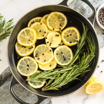 A pot filled with water, lemon slices, peppercorns, rosemary sprigs, and vanilla extract
