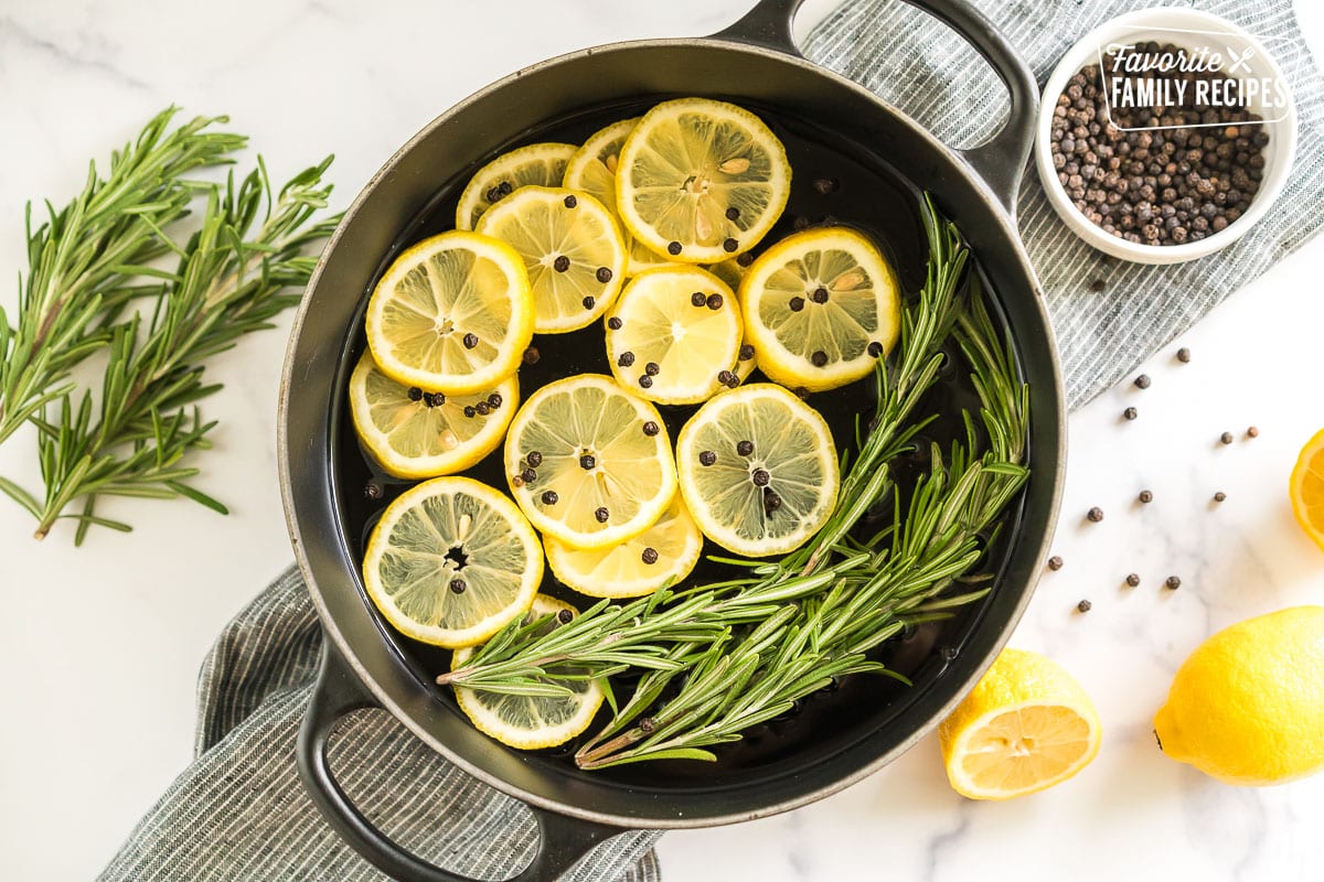 A pot filled with water, lemon slices, peppercorns, rosemary sprigs, and vanilla extract