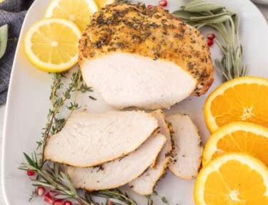 Sliced Turkey Breast Roast on a platter with citrus slices and herbs.